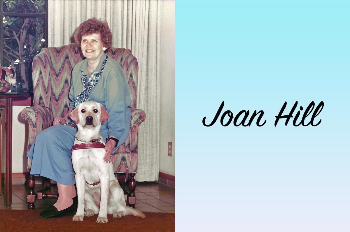 Joan sits smiling in a comfortable chair with an adorable golden guide dog sitting attentively at her side. 