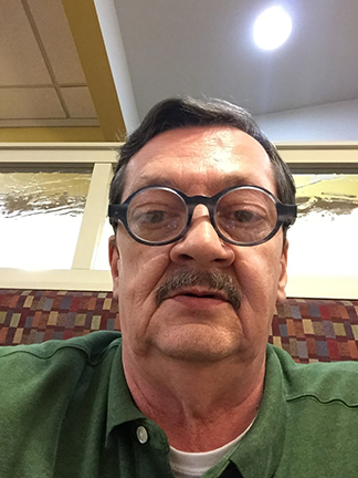 Richard, wearing a green shirt and glasses, takes a selfie.
