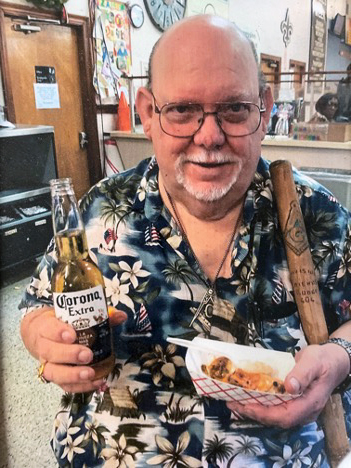 Terry sits in a Hawaiian shirt, holding a fresh beer and a basket of food.
