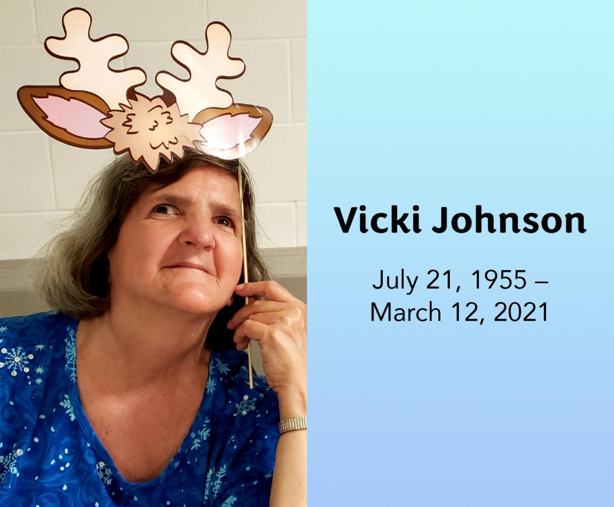 Vicki dressed in holiday clothes smiles as she holds a cutout of deer antlers at the top of her head. Vicki Johnson, July 21, 1955 - March 12, 2021.
