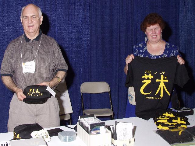 Mike Mandel and Nancy Marie-Luce hold up Friends-in-Art items (a hat and a T-
shirt) at the booth in the exhibit hall.