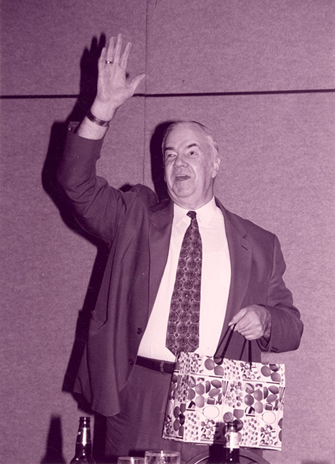 Oral Miller stands, waves, and thanks the convention for the beautiful retirement gifts, which included a trip for two to Vienna, Austria. In his left hand is a gift bag, gaily decorated with a balloon print. 